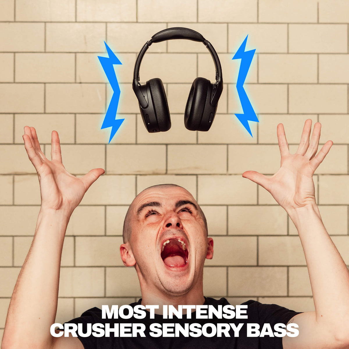 True Black | A man with his hands raised in front of a beige tiled wall, looking upward with an open mouth, with a pair of black Crusher 720 over-ear headphones floating above him and blue lightning bolts indicating sound. White text at the bottom reads 'MOST INTENSE CRUSHER SENSORY BASS'.