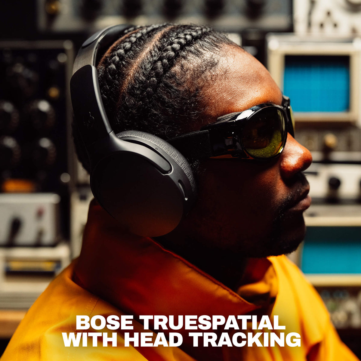 True Black | A man in profile wearing black Crusher 1080  headphones with head tracking and dark sunglasses, set against a blurred studio background with audio equipment. White text at the bottom reads 'BOSE TRUESPATIAL WITH HEAD TRACKING'.