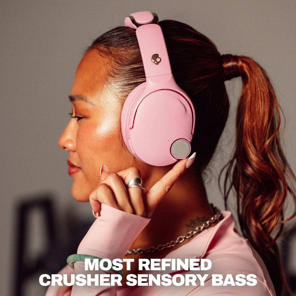 Candy | A woman in profile wearing light pink over-ear headphones with a small skull logo on the headband. The image includes text at the bottom reading 'MOST REFINED CRUSHER SENSORY BASS.