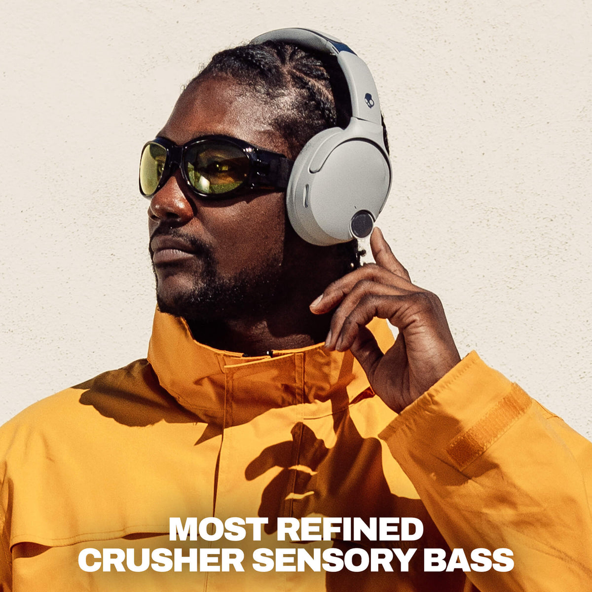 Cement | A man wearing white Crusher 1080 over-ear headphones and dark sunglasses, dressed in a bright yellow jacket, with the text 'MOST REFINED CRUSHER SENSORY BASS' at the bottom.