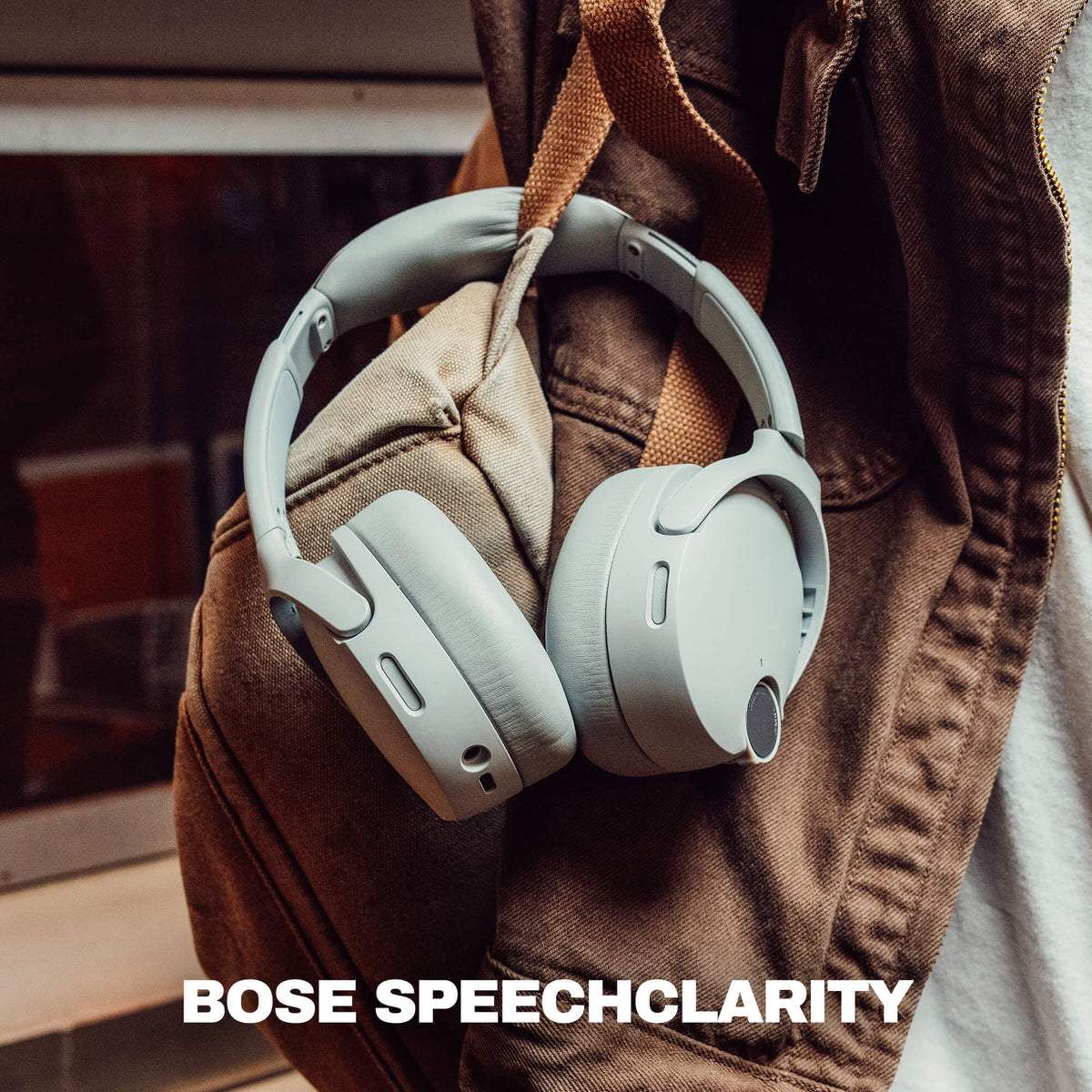 Cement | Light gray crusher 1080 over-ear headphones hanging from a brown jacket, with the text 'BOSE SPEECHCLARITY' at the bottom.