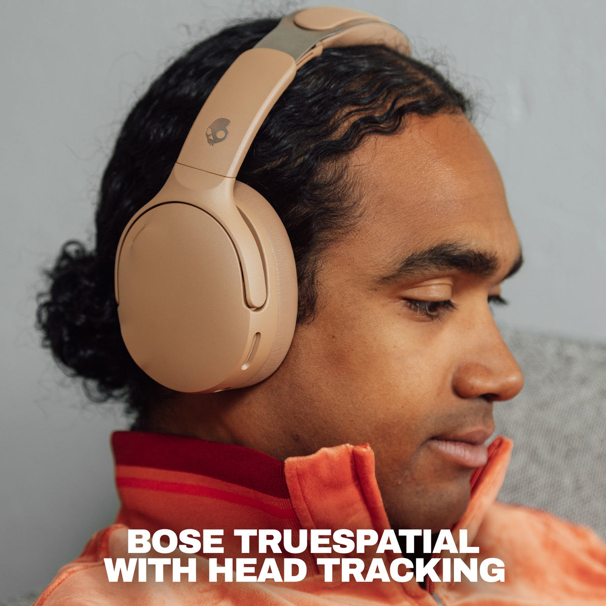 Primer | A man wearing beige Skullcandy 1080 with Bose TrueSpatial over-ear headphones with head tracking, shown in profile against a neutral gray background with promotional text at the bottom.