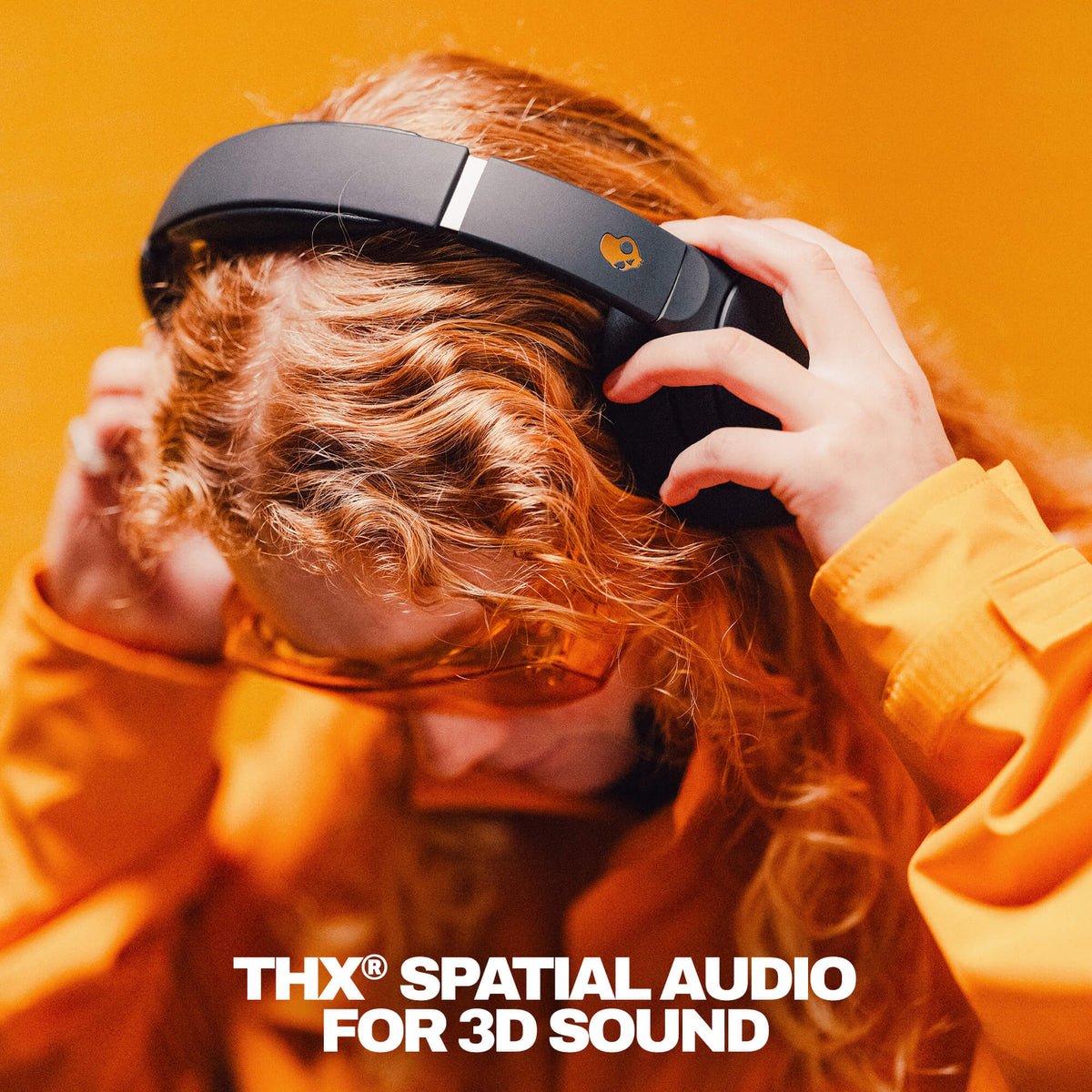 True Black | Person wearing black Crusher 720 headphones with THX Spatial Audio branding against an orange background