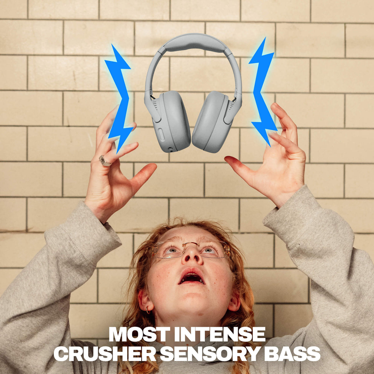 Cement | Person holding up Crusher 720 headphones with blue lightning bolts and 'MOST INTENSE CRUSHER SENSORY BASS' text against a tiled wall.